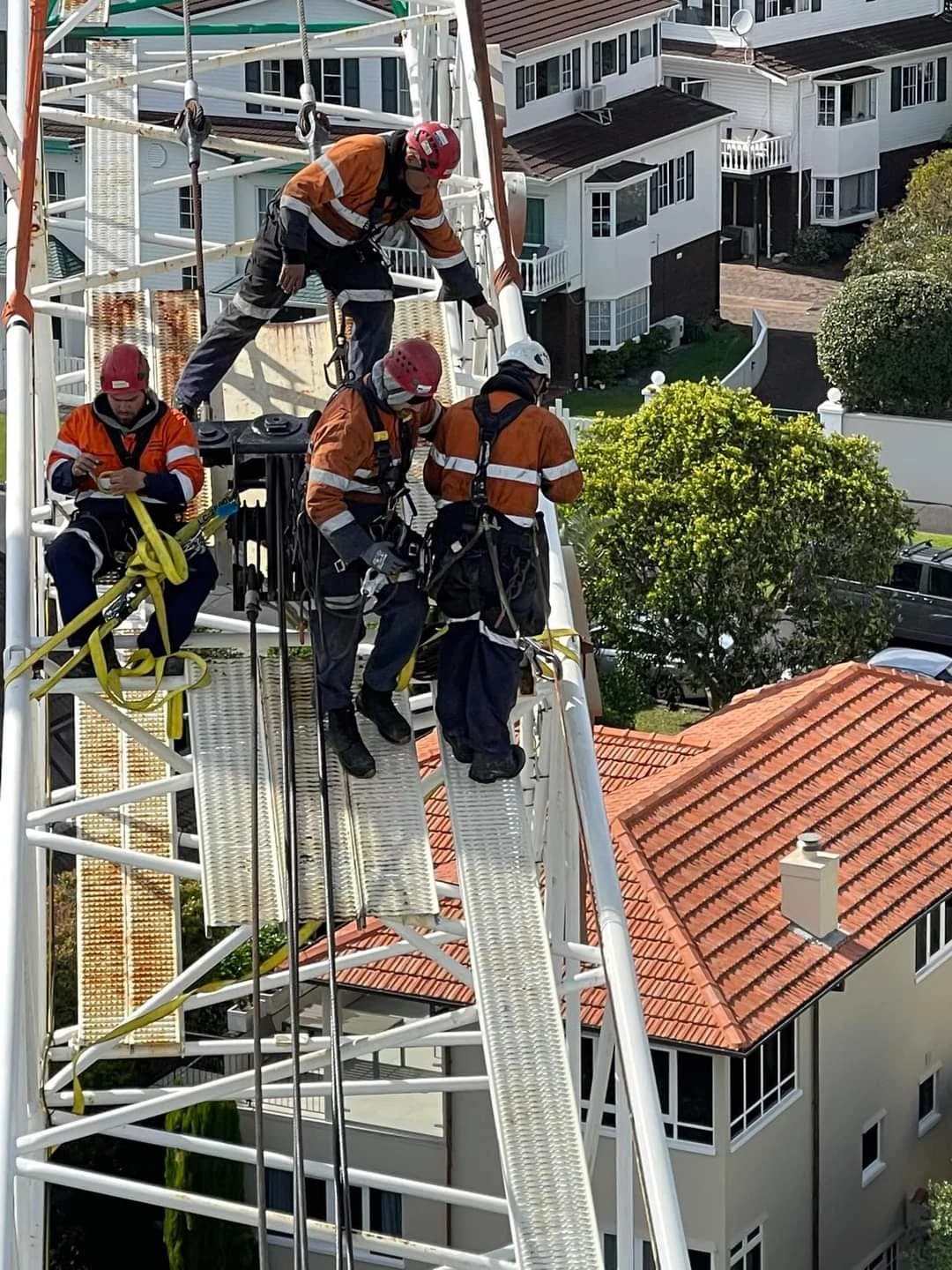 Four crew in hi-vis and harnesses on an access tower above suburban rooftops.