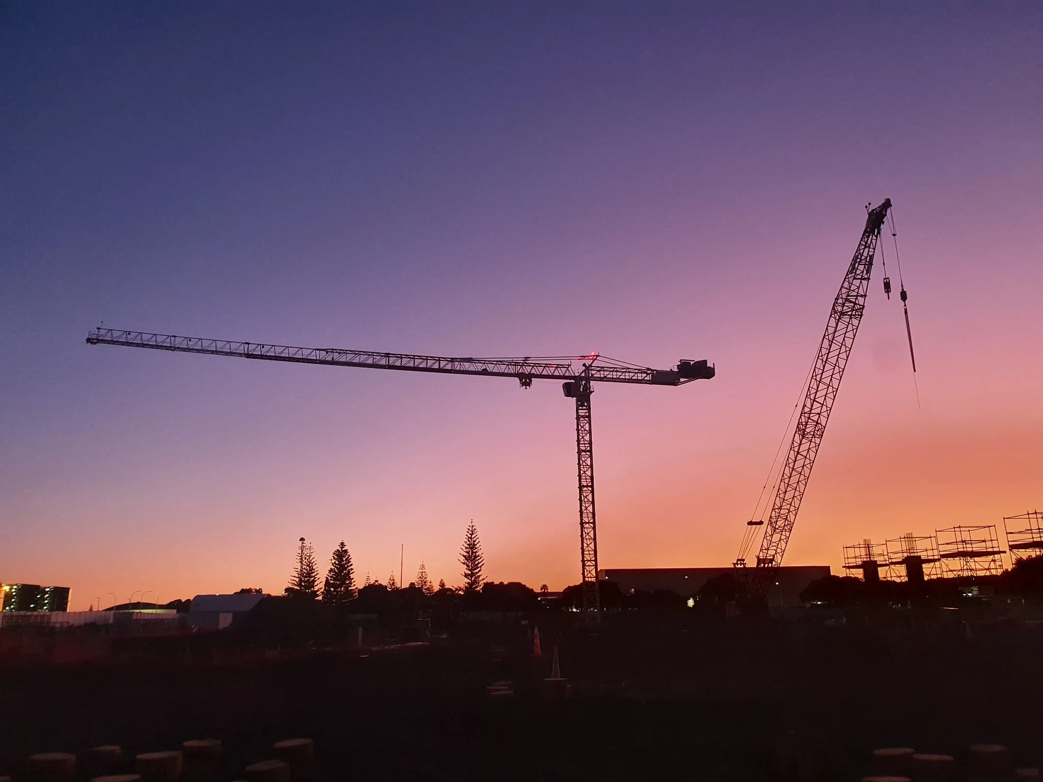 Tower cranes silhouetted against a pink and purple sunset sky.