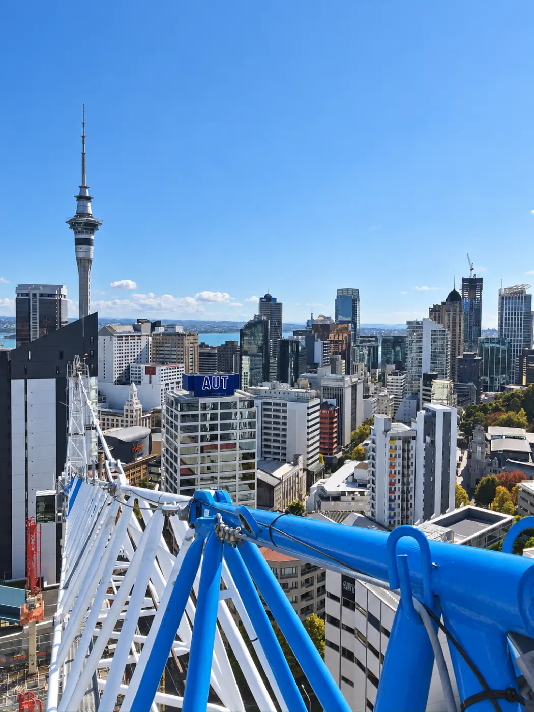 A blue crane jib reaching across the Auckland skyline towards the Sky Tower.